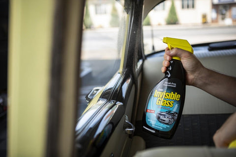 Person holding a bottle of Invisible Glass cleaner inside a car.
